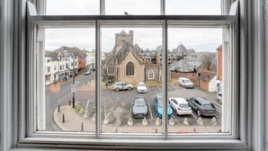A view through a window of a street with parked cars, a church, and residential buildings. - 1 Bed in Lewes (oc-n29713) (Lewes)