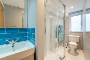 Un baño moderno con cabina de ducha de vidrio, inodoro blanco y zona de lavamanos con azulejos azules.