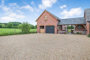 A brick building with a gravel driveway, a covered porch, and a fenced green field in the background. - 1 Bed in Abbeydore (oc-l29485) (Abbey Dore)