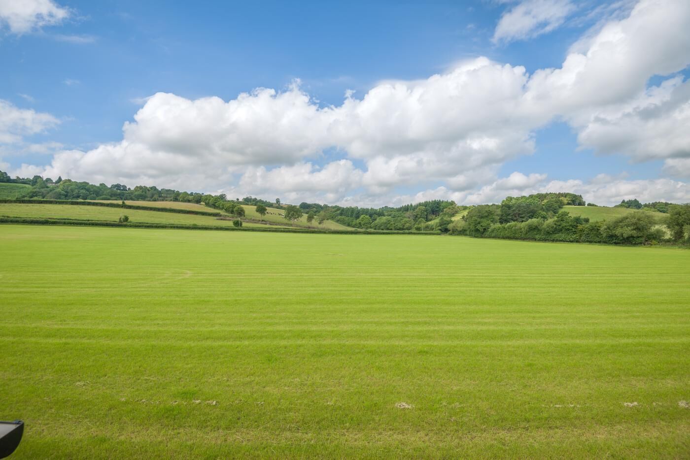 A vast green field with a clear sky and scattered clouds.
