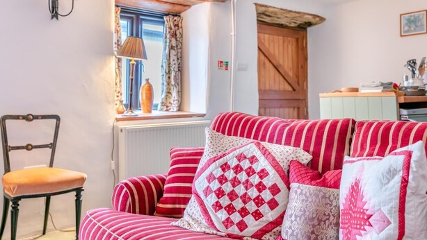 Een gezellige kamer met een gestreepte bank, een stoel, een raam met gordijnen en een houten deur.