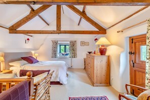 A cozy bedroom with a bed, bedside table, lamp, and a view of the outdoors through a window.