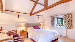 Een slaapkamer met een bed, nachtkastjes, een raam met gordijnen en zichtbare houten balken.