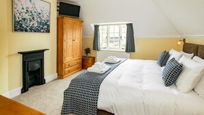 Een slaapkamer met een bed, een houten garderobe, een open haard, een raam met gordijnen en een schilderij aan de muur.