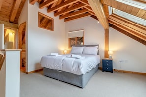 Ein Schlafzimmer mit einem Bett, Nachttischen, einer Holzbalkendecke und einem Fenster.