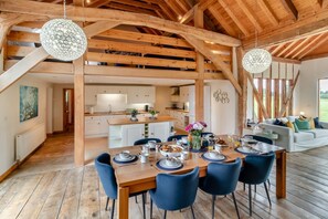A spacious dining area with a wooden table set for a meal, surrounded by blue chairs, under a wooden ceiling with exposed beams. - 3 Bed in Frostenden (oc-g29705) (Frostenden)