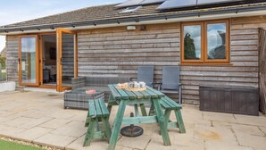 Una cabaña de madera con un patio, una mesa y sillas, y un techo con paneles solares.