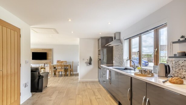 Una cocina moderna con un amplio ventanal, un comedor con mesa y sillas, y una sala de estar con sofá y televisión.