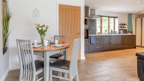 Une cuisine moderne avec des meubles gris, une porte en bois et un coin repas comprenant une table et des chaises en bois.