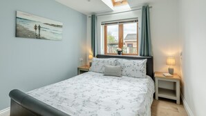 Une chambre avec un puits de lumière, un lit avec une literie à motifs floraux, une table de chevet avec une lampe et une fenêtre avec des rideaux.