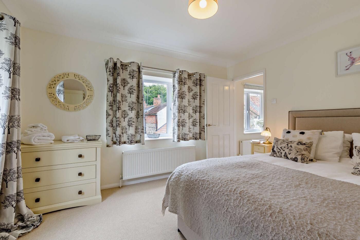 Une chambre à coucher avec un lit, une commode, un miroir et une fenêtre avec des rideaux.