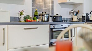 A modern kitchen with white cabinets, a stainless steel oven, and a countertop with various kitchen items and fresh vegetables. - 3 Bed in Castle Acre (oc-f29723) (Castle Acre)