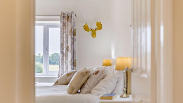 A bedroom with a bed, two bedside lamps, a window with curtains, and a wall-mounted decoration. - 3 Bed in Castle Acre (oc-f29723) (Castle Acre)
