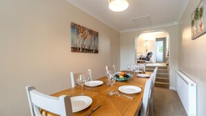 A dining area with a wooden table set for four, white chairs, and a bowl of fruit. - 3 Bed in Castle Acre (oc-f29723) (Castle Acre)