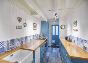 A narrow kitchen with blue and white tiles, wooden countertops, and a blue door. - 3 Bed in Staithes (oc-g29738) (Staithes)