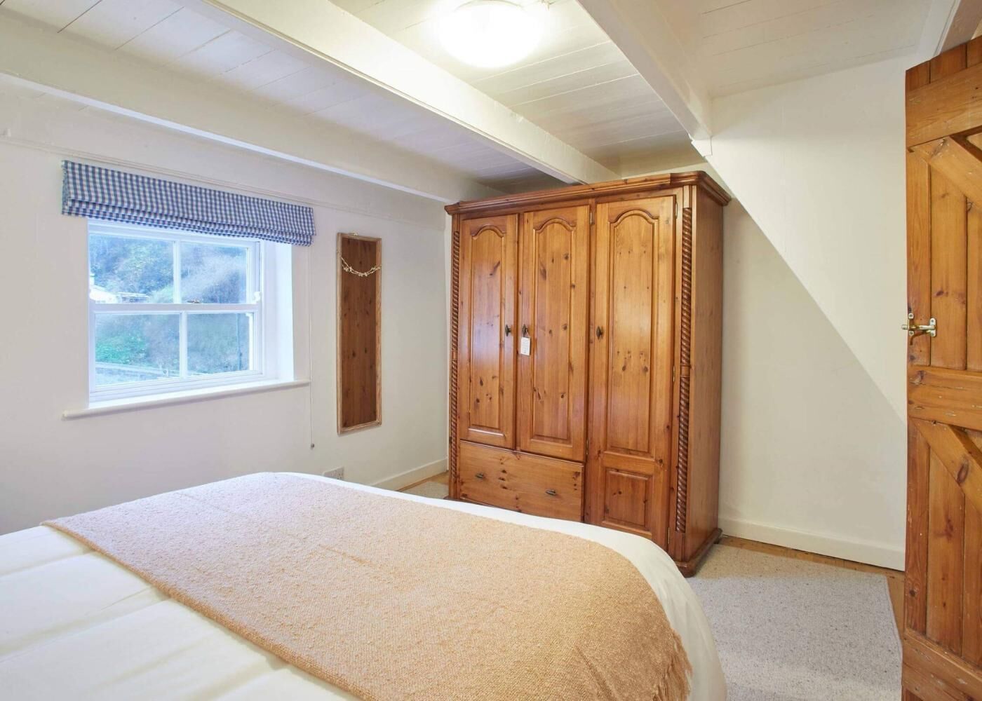 Quarto com cama, guarda-roupa de madeira, janela com vista e teto inclinado.