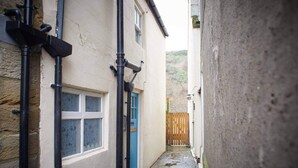 A narrow alleyway with a blue door and a window, flanked by buildings with visible plumbing. - 3 Bed in Staithes (oc-g29738) (Staithes)