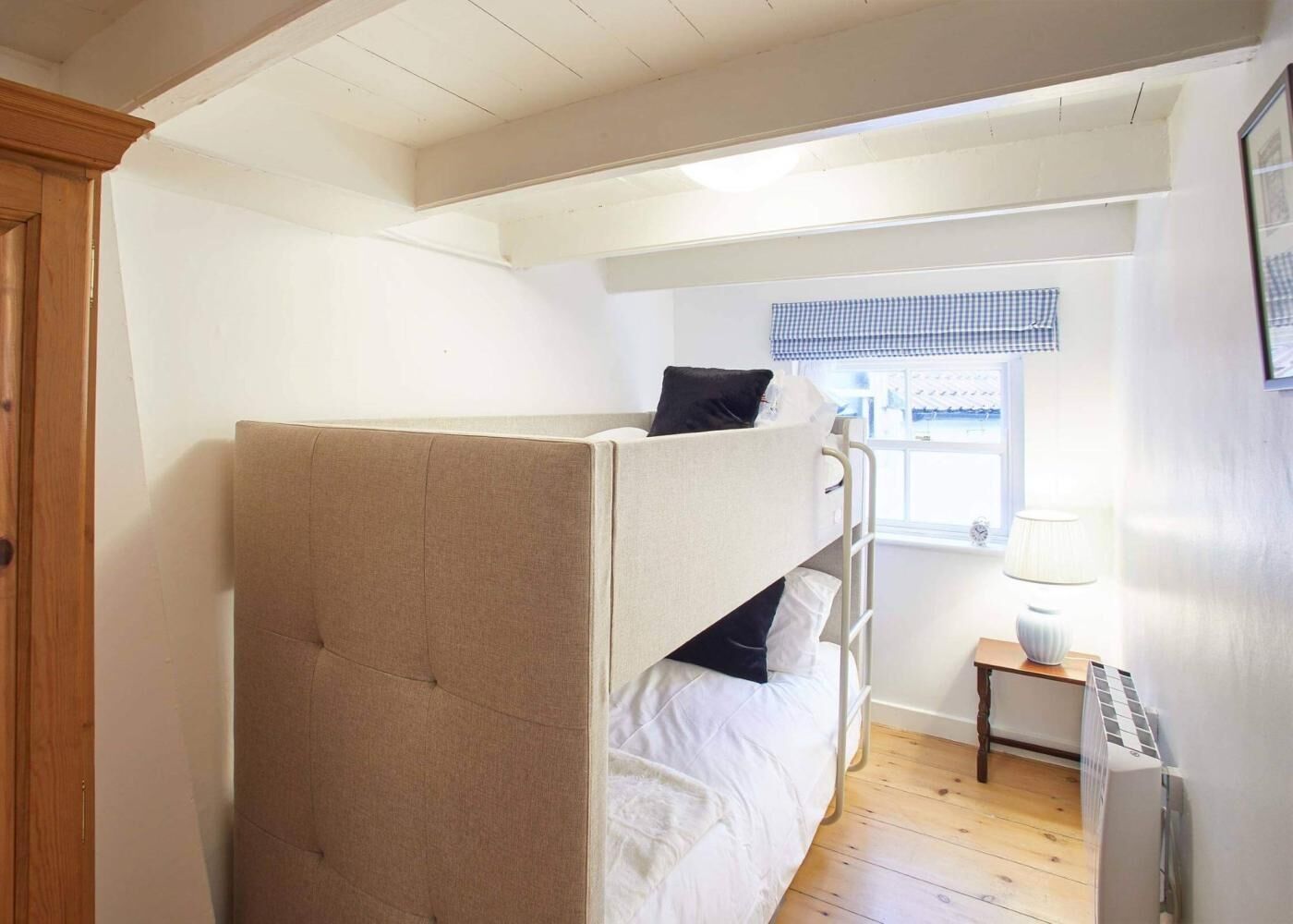 A bunk bed with a headboard, a bedside table with a lamp, and a window with a checkered blind.