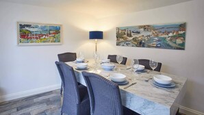 A dining area with a marble table set for six, surrounded by wicker chairs, with two paintings on the walls. - 3 Bed in Staithes (oc-g29738) (Staithes)