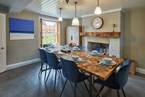A dining room with a wooden table set for six, blue chairs, a fireplace, and a clock on the wall. - 4 Bed in Egton (oc-a29734) (Egton)