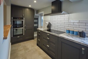 A modern kitchen with dark cabinetry, a marble countertop, and built-in ovens. - 4 Bed in Egton (oc-a29734) (Egton)