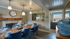 Zona pranzo con tavolo in legno apparecchiato per sei persone, sedie blu e lampade a sospensione. Un orologio è montato sulla parete sopra il tavolo.