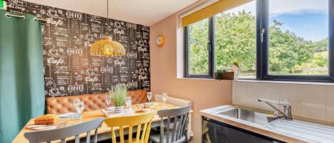 Cocina compacta con ventana, zona de comedor con banco y una pared decorada con motivos de café.