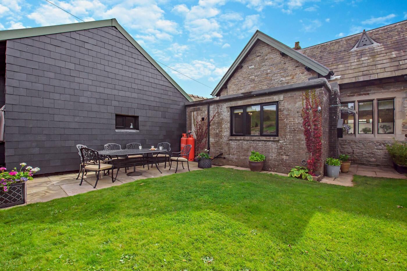 A backyard with a dining table and chairs, a brick building, and a stone building with a window.