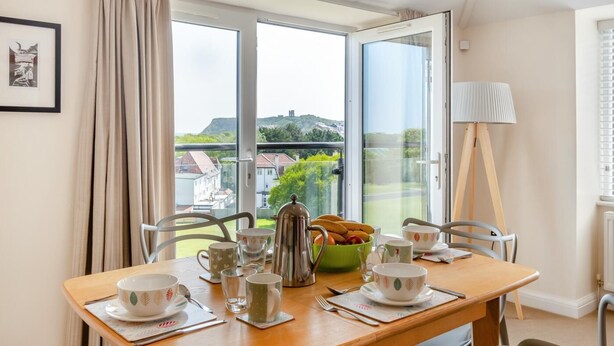 Un coin repas avec une table mise pour le petit-déjeuner, une vue sur la ville à travers de grandes fenêtres et un radiateur au mur.
