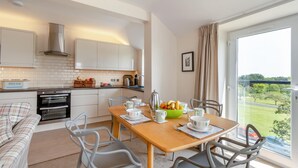 Une cuisine moderne avec des meubles blancs, une table à manger accompagnée de chaises, et une vue sur la verdure à l’extérieur.