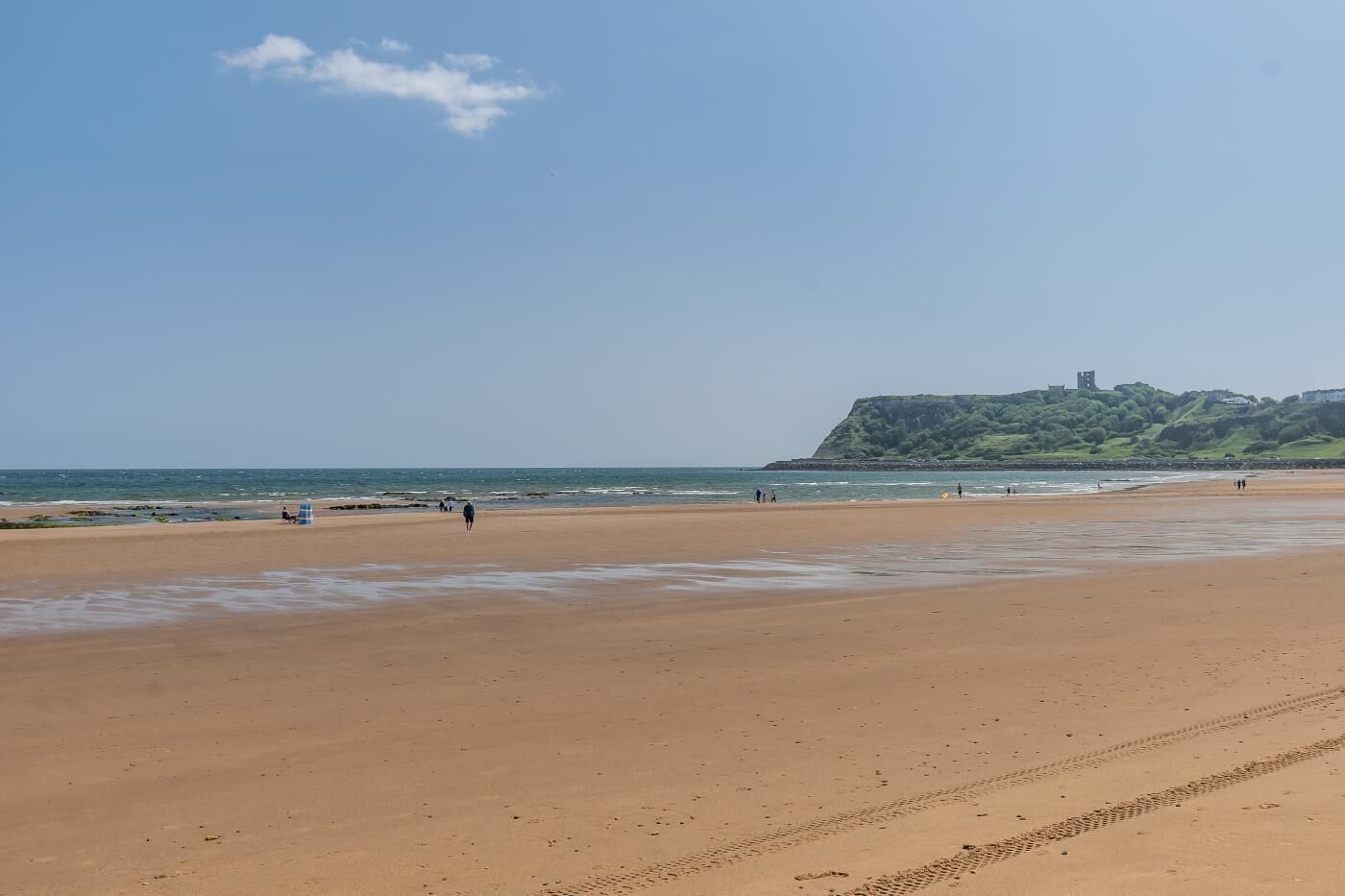 A wide sandy beach with footprints and a few people walking.