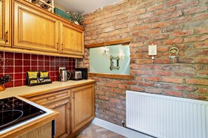 A kitchen with wooden cabinets, a tiled backsplash, a brick wall, a window, and a radiator. - 1 Bed in Luddendenfoot (oc-b29721) (Halifax)