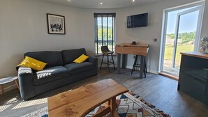 Uma sala de estar com um sofá cinza, mesa de centro de madeira e uma TV fixada na parede.