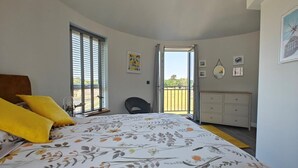 Quarto com cama, uma cadeira, cômoda e varanda.