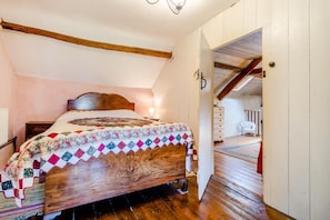 A bedroom with a wooden bed, a quilt, a nightstand, and a white dresser.