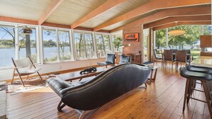Un vaste espace intérieur doté d’un plancher en bois, de grandes fenêtres et d’une vue sur un lac. On y trouve des canapés et des fauteuils en cuir, ainsi qu’une table à manger.