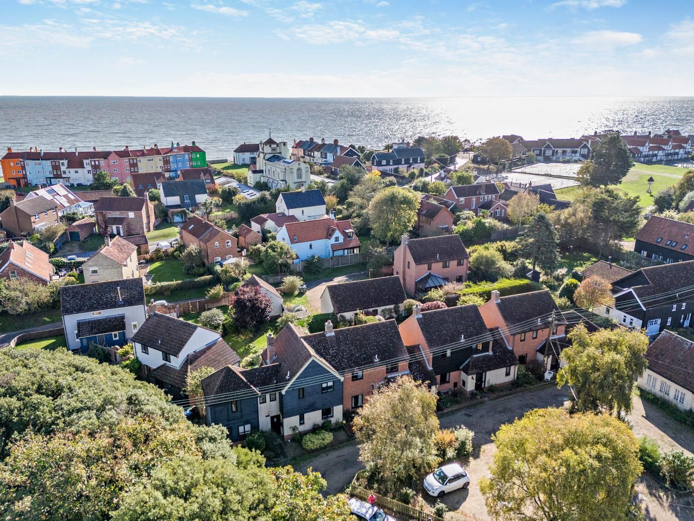 Luftaufnahme einer Küstenwohngegend mit Häusern, Grünflächen und Blick aufs Meer.
