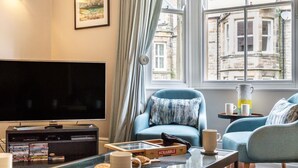 Un salon comprenant un téléviseur, un canapé, une table basse et une fenêtre donnant sur des immeubles.