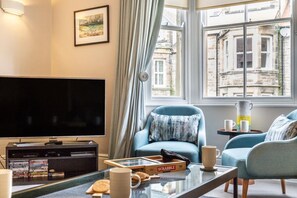 Ein Wohnzimmer mit Fernseher, einer Couch, einem Couchtisch und einem Fenster mit Blick auf Gebäude.