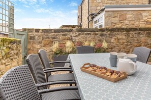 Eine Terrasse mit Korbstühlen und einem für Tee gedeckten Tisch, umgeben von Steinmauern und Pflanzen.