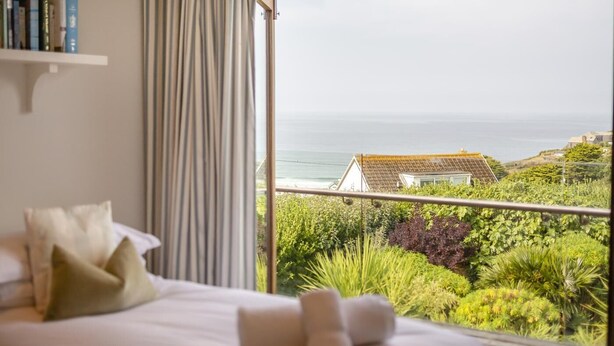 Une chambre à coucher avec un lit, des oreillers et une vue sur la mer et la verdure.