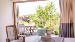 Une chambre avec un lit, une chaise, une table et une vue sur un jardin avec des plantes et un palmier.