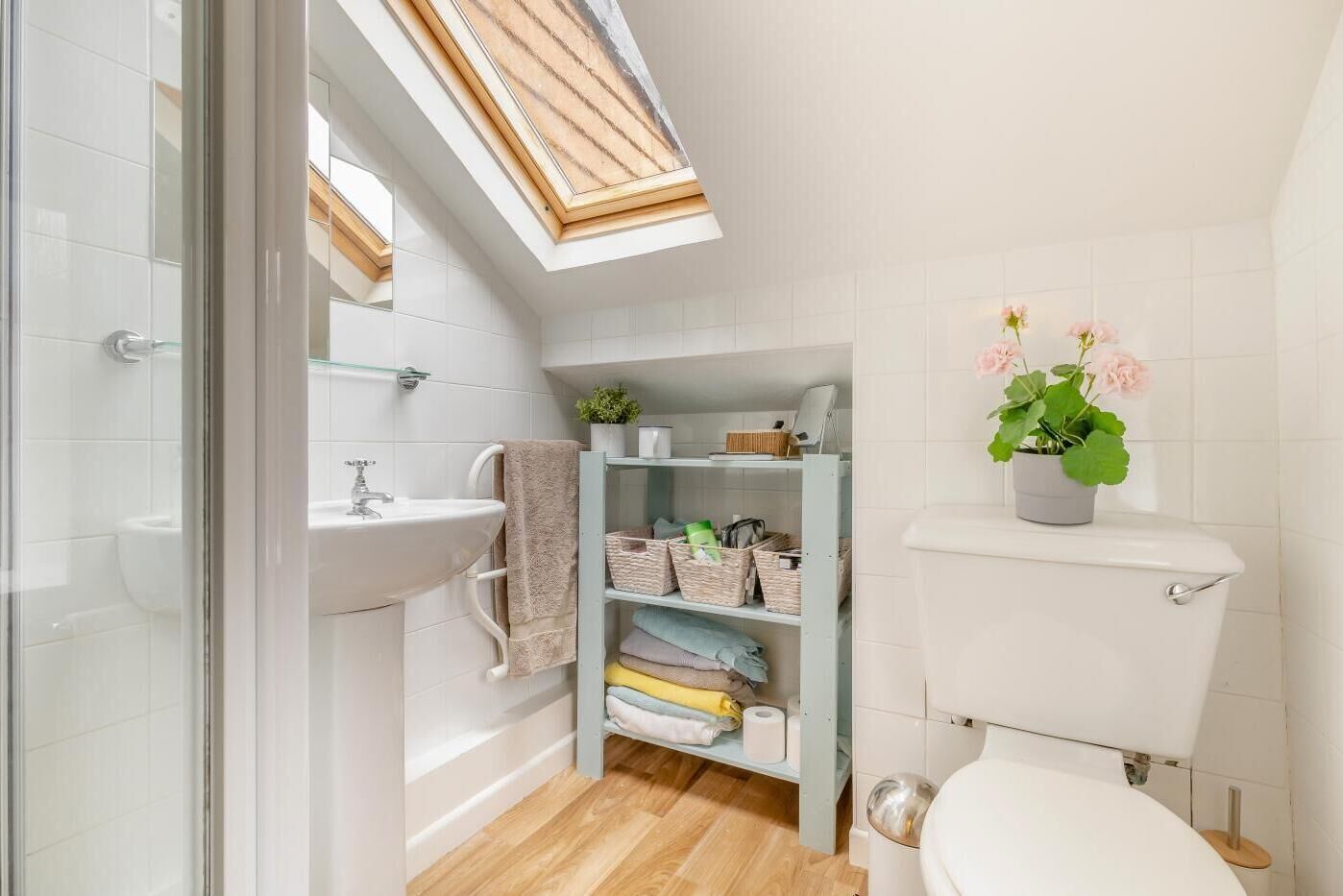 A compact bathroom with a skylight, a white sink, a toilet, and a shelf with toiletries.