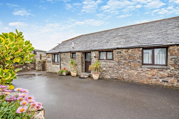 A stone building with a sloped roof, multiple windows, and a paved courtyard. - 2 Bed in Padstow (oc-w3658) (Treyarnon Bay)