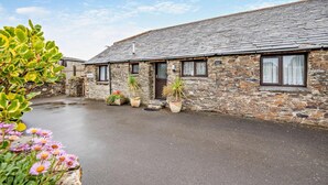 A stone building with a sloped roof, multiple windows, and a paved courtyard. - 2 Bed in Padstow (oc-w3658) (Treyarnon Bay)