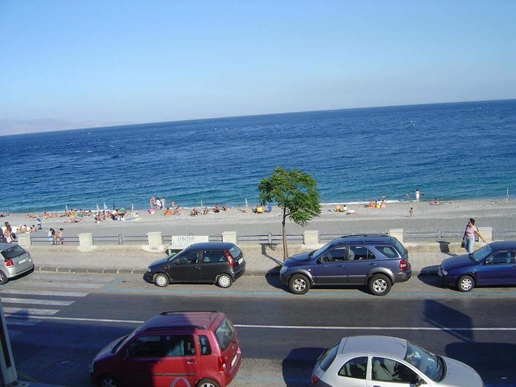 A coastal road with parked cars and a beach in the background.