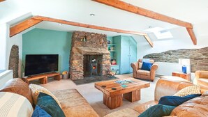 A cozy living room with a stone fireplace, leather sofas, a wooden coffee table, and a television. - 3 Bed in St. Ervan (oc-t29660) (Saint Ervan)