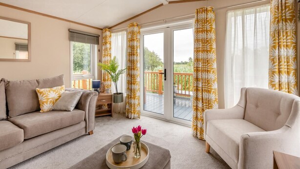 Een ruime woonkamer met een bank, fauteuil en salontafel met een dienblad vol bekers en bloemen.