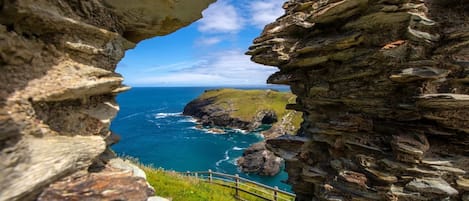 A coastal view through a stone archway with a grassy path and railing.