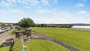 A grassy field with a large tent, a stone wall, and parked cars. - 2 Bed in Delabole (oc-r29780) (Delabole)